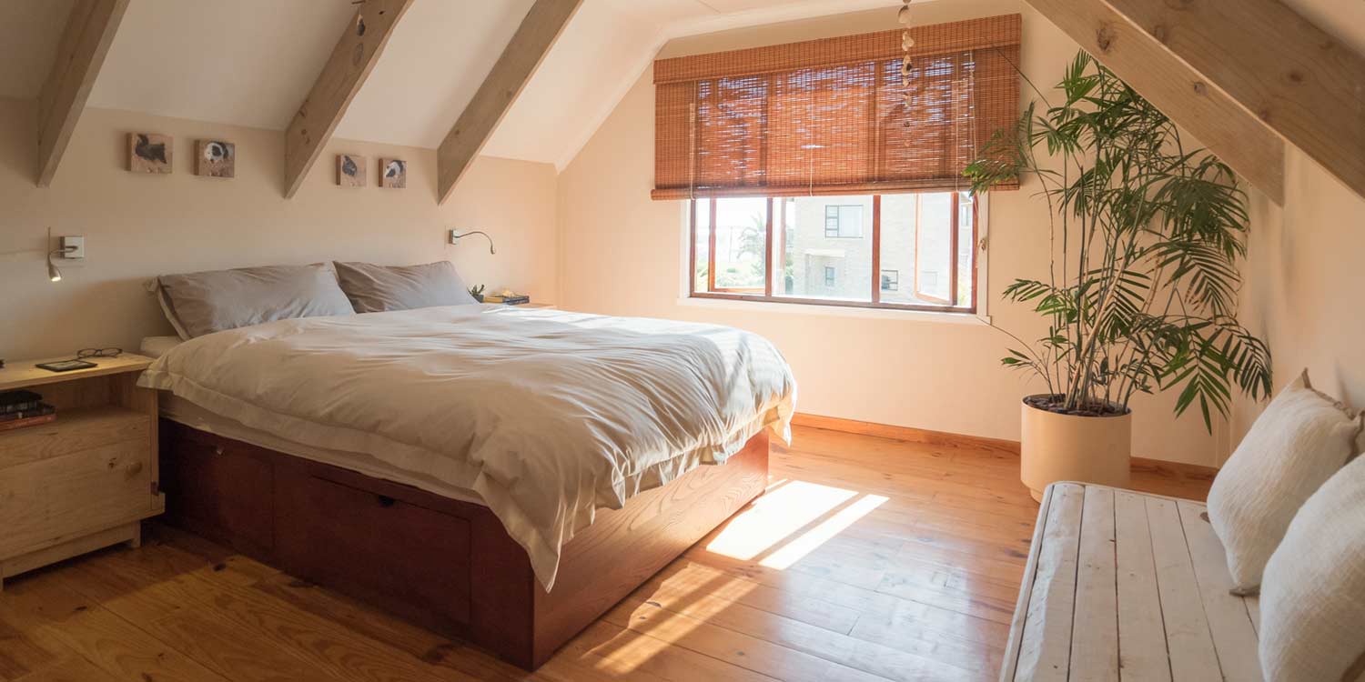 A bright bedroom in a rental apartment with sunlight streaming through a window, illuminating the bed and simple furnishings.