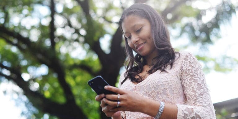 A woman is texting on her smartphone with trees in the background