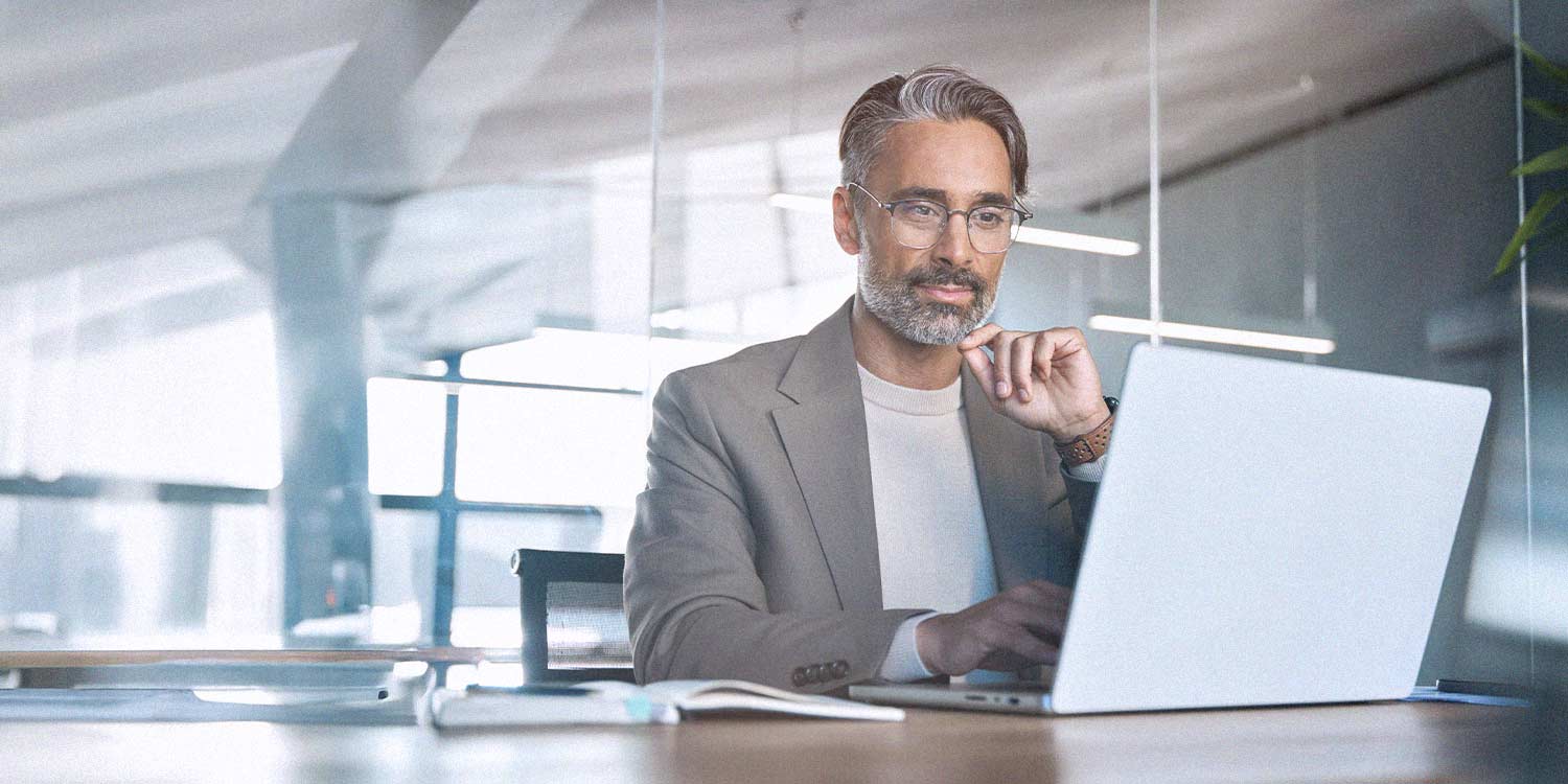 An older man looks at his laptop in an office environment