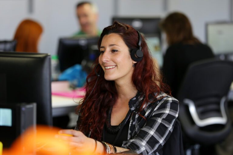 A contact center agent wearing a headset takes calls from customers while three more agents work in the background