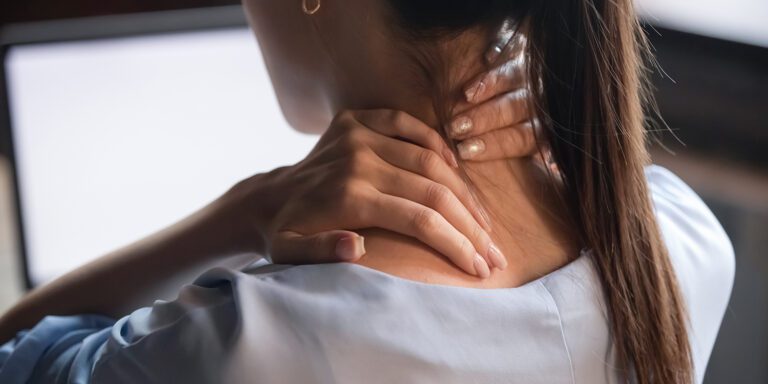 A woman grabs the back of her neck as if she is feeling pain or discomfort