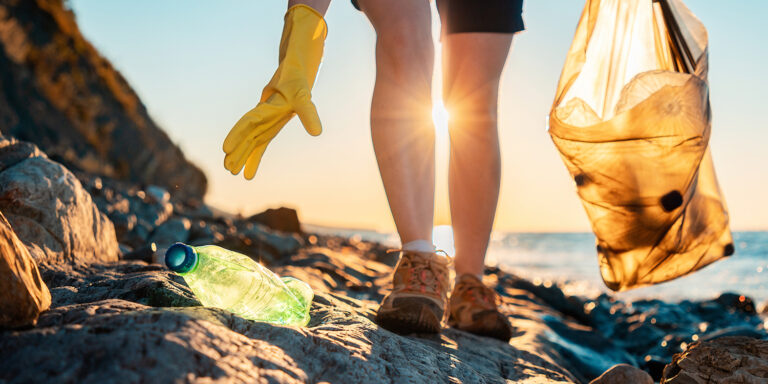 Person wearing a glove collecting plastic garbage on a beach