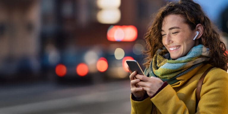 A smiling young female uses her smartphone with a city setting in the background