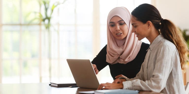 Two women are working together at a desk with a laptop