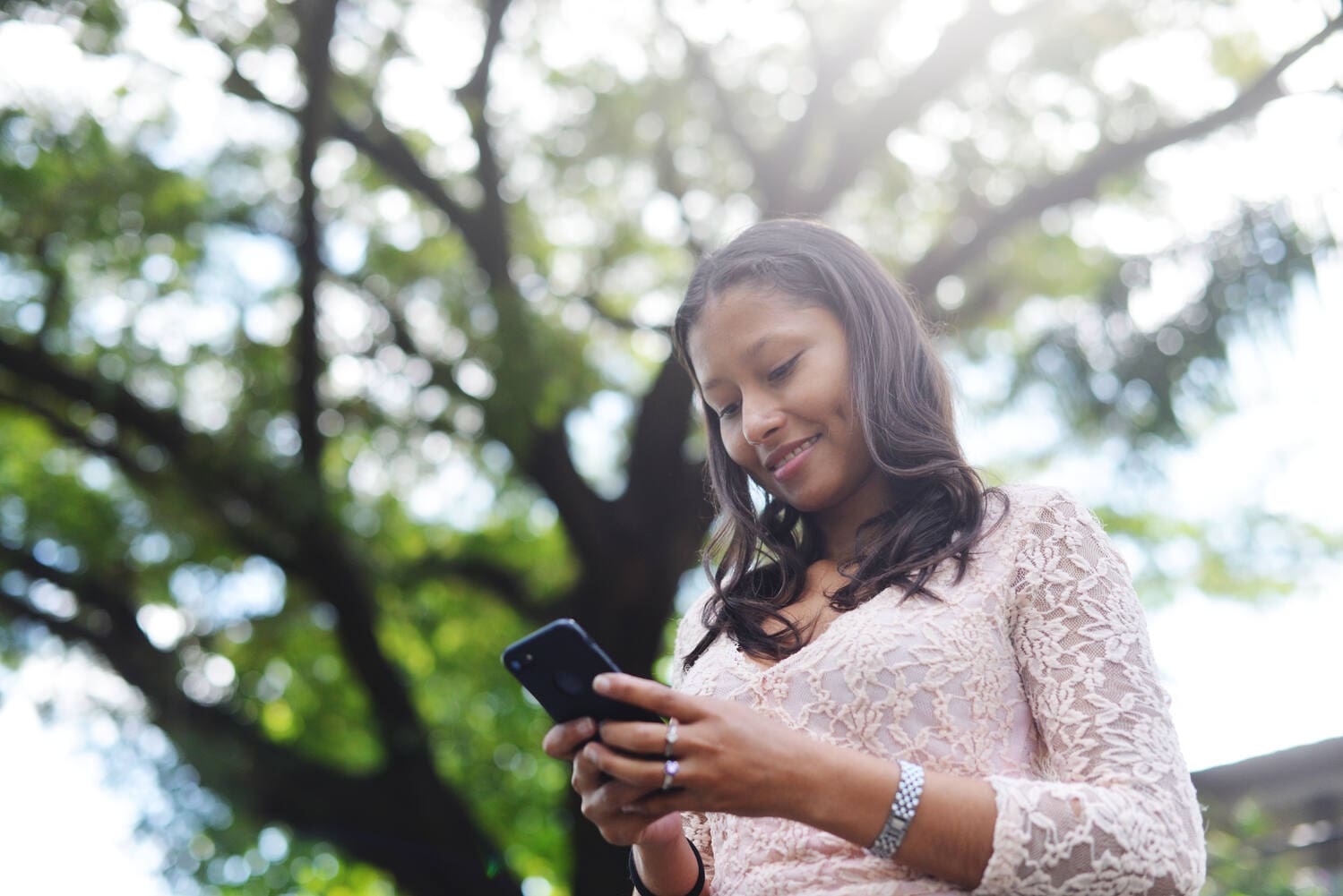 A woman is texting on her smartphone with trees in the background