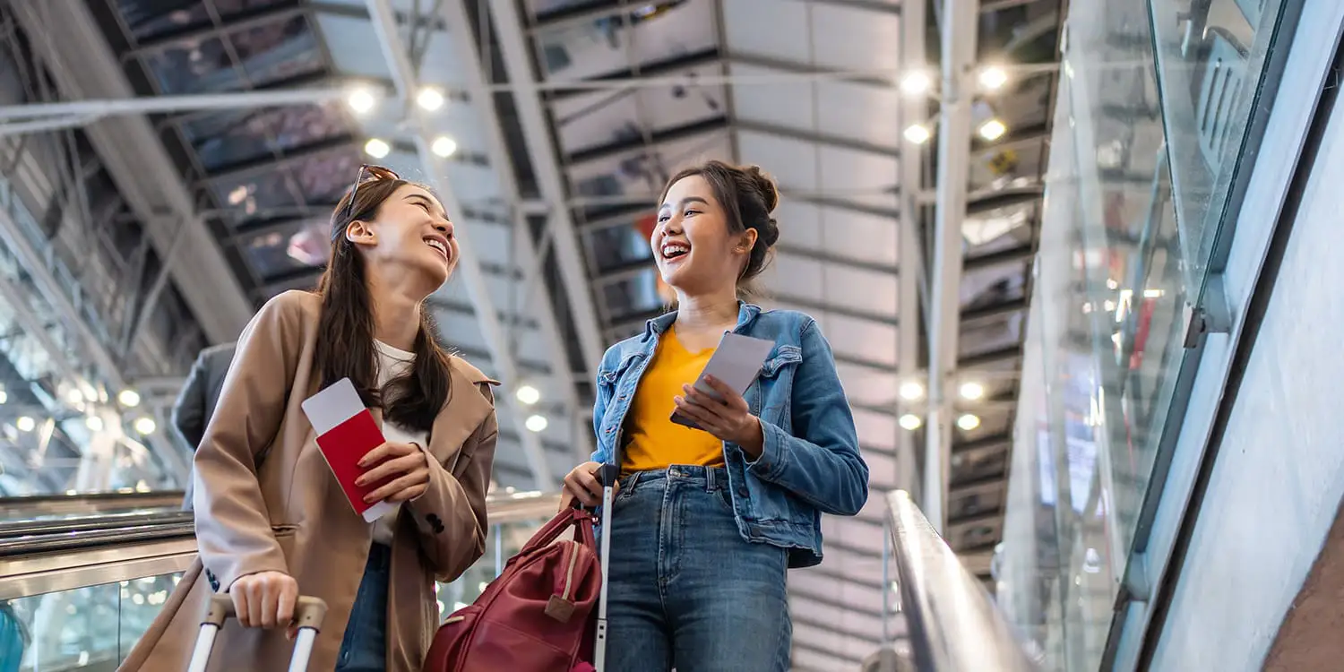 Two female travelers are on an escalator in an airport