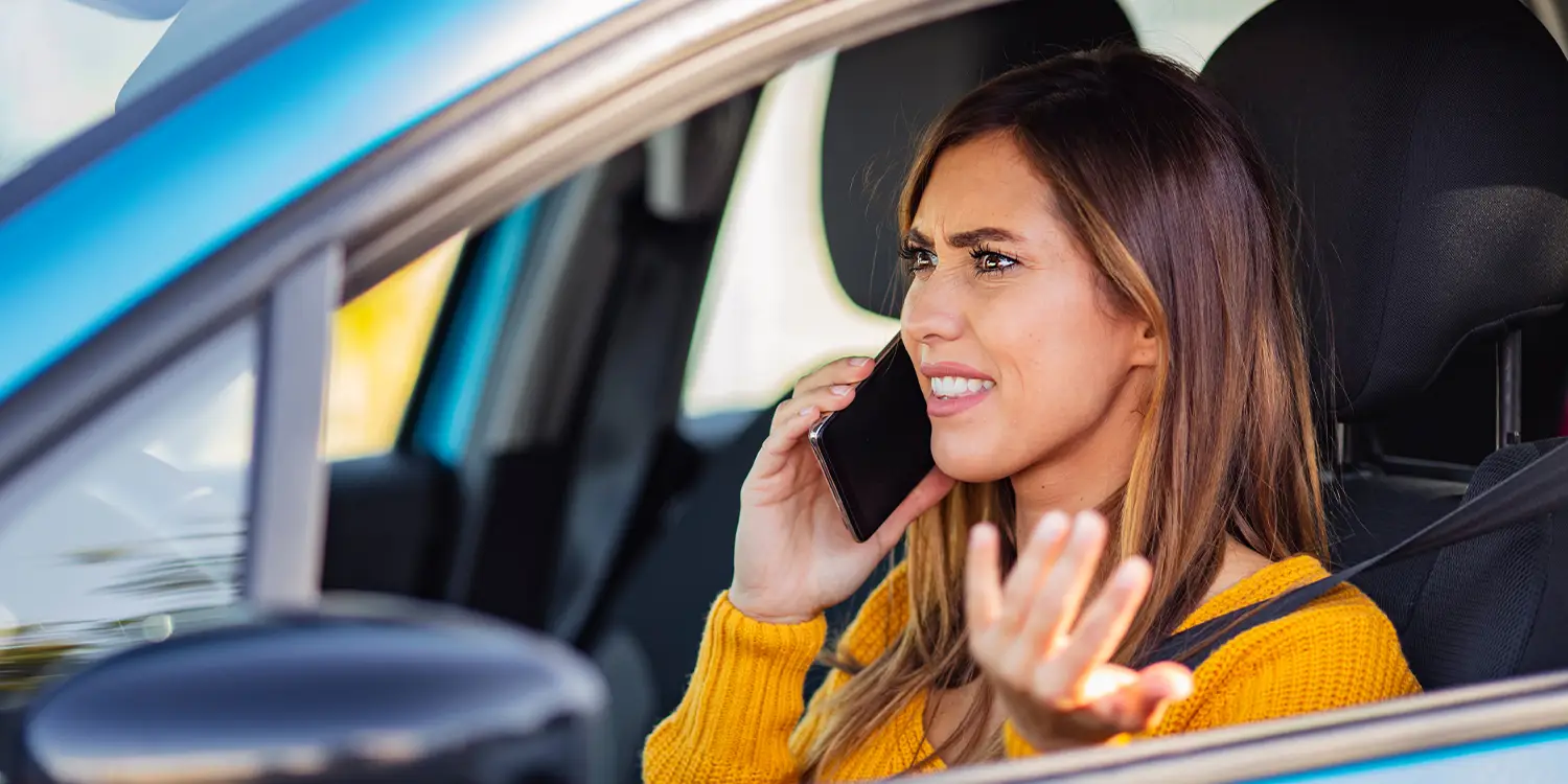 A woman sitting in a car looks upset while on a call on her mobile phone