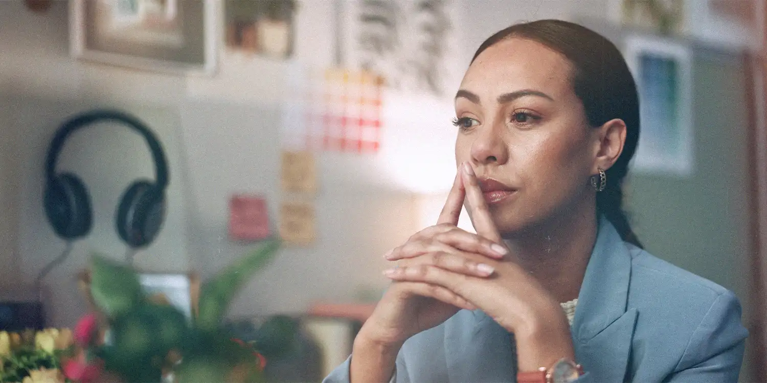 A woman looks as if she is planning or in deep thought as she looks forward with her hands clasped in from of her chin