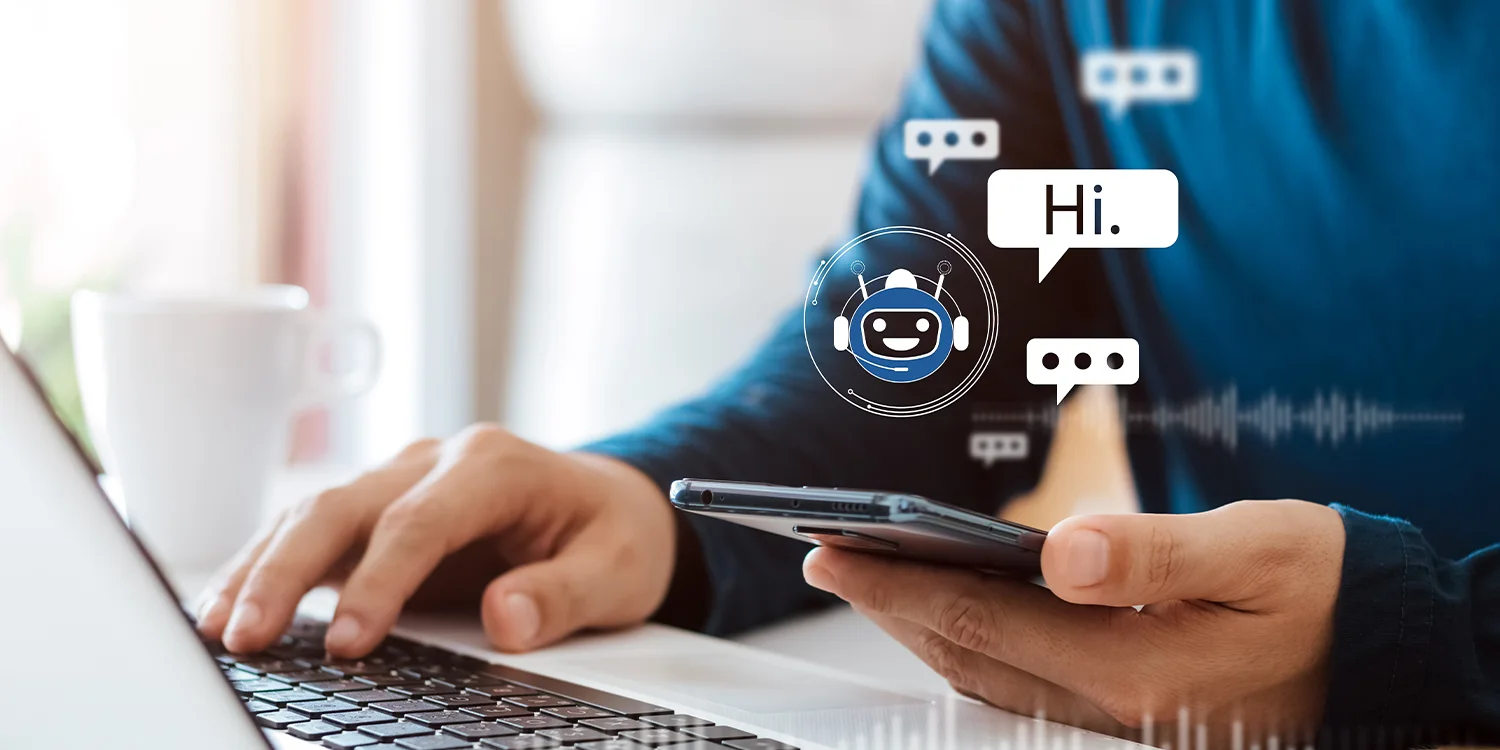 Closeup of a man interacts with a chatbot on a smartphone while typing on a laptop