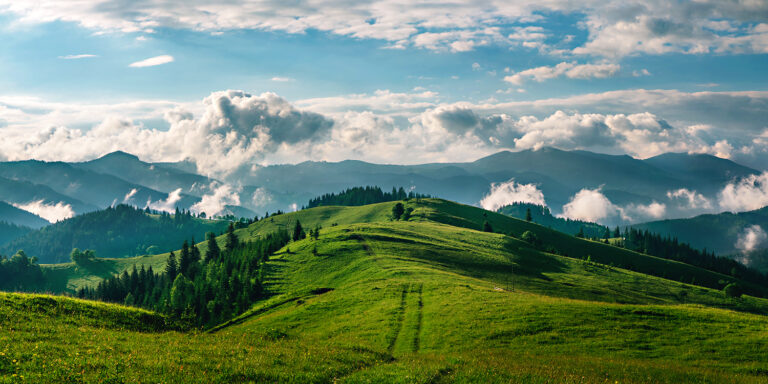 View of green, hilly landscape with blue sky and white puffy clouds