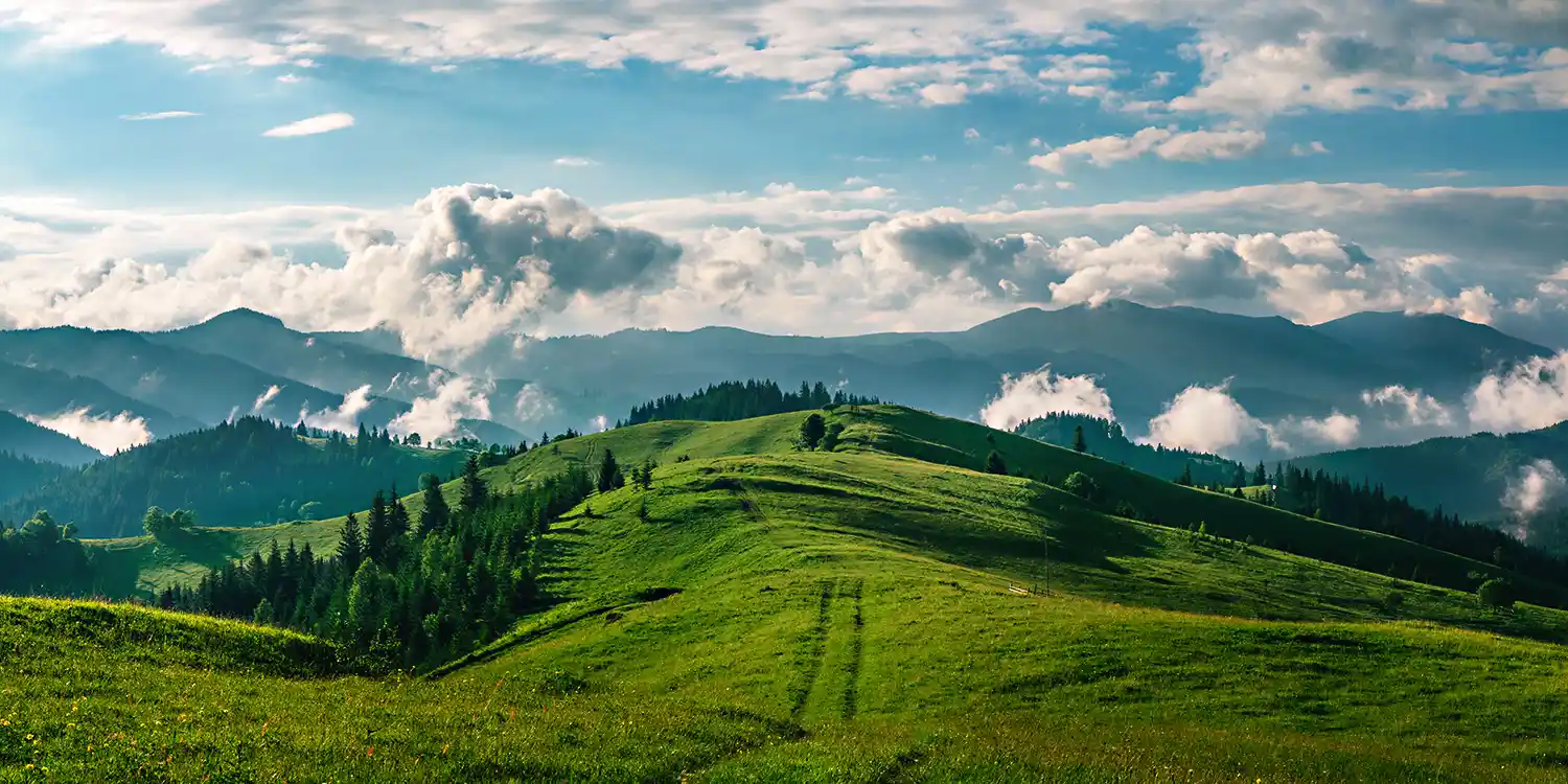 View of green, hilly landscape with blue sky and white puffy clouds