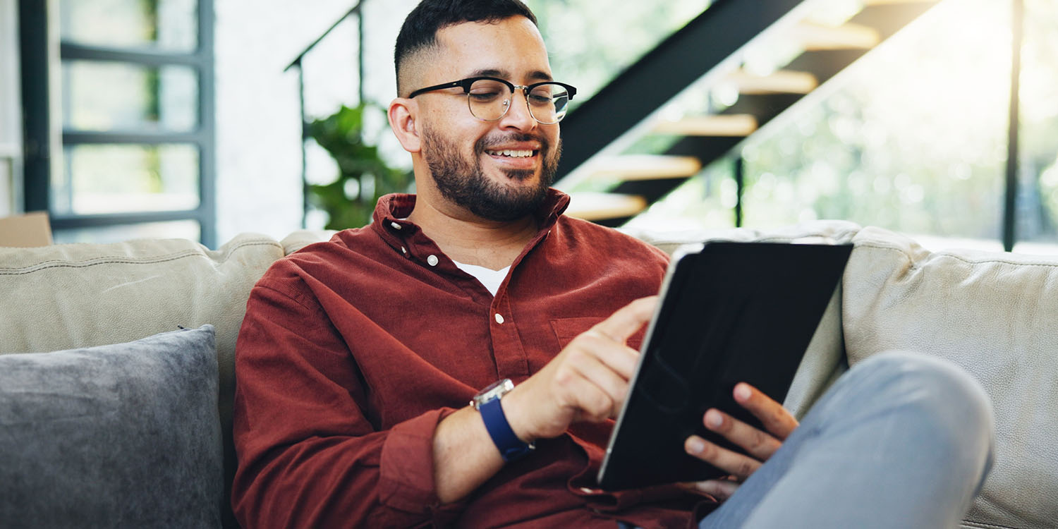 A young man looks at a tablet while sitting on a sofa