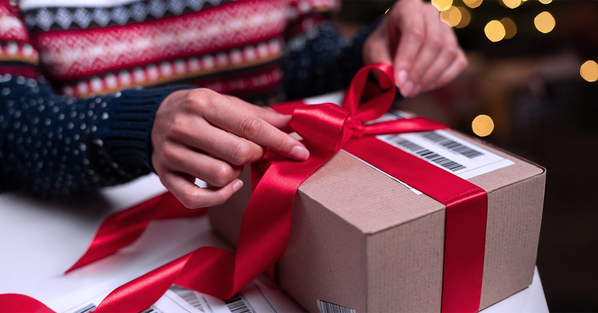 Closeup of a person opening a holiday present — a brown box with a red bow