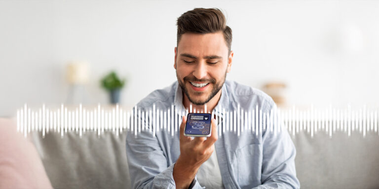 Front view of a man sitting on a sofa and engaging with a voicebot on a smartphone
