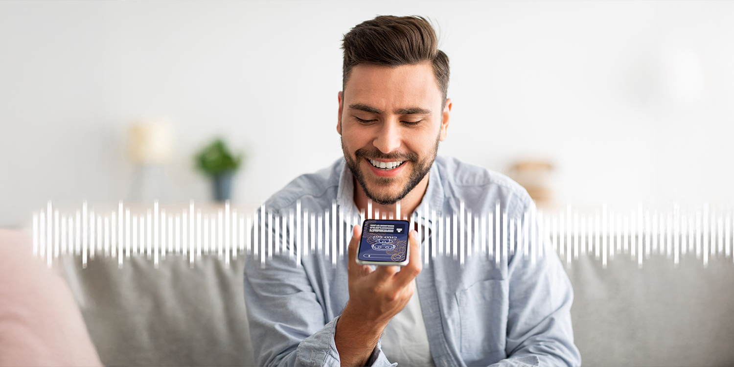 Front view of a man sitting on a sofa and engaging with a voicebot on a smartphone