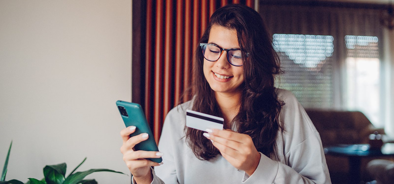 A female looks at a credit card while holding a smartphone