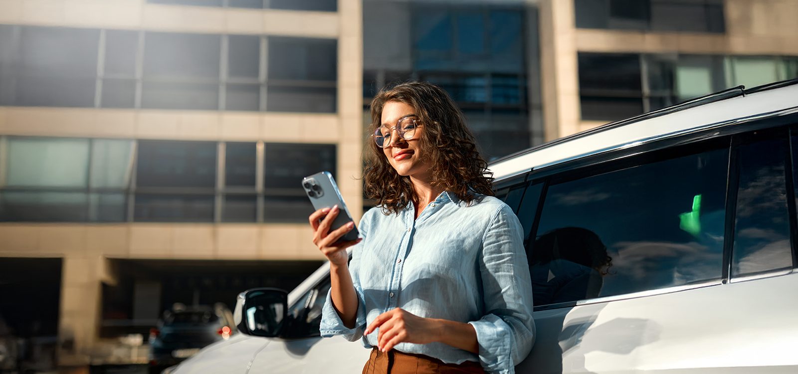A woman looks at her smartphone while standing outside beside a minivan