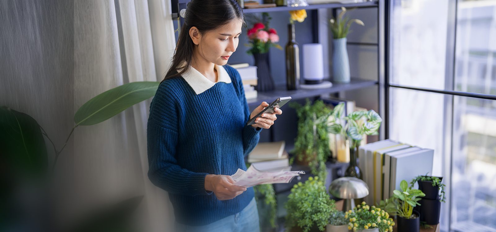 A woman standing and holding a bill makes a call on her smartphone
