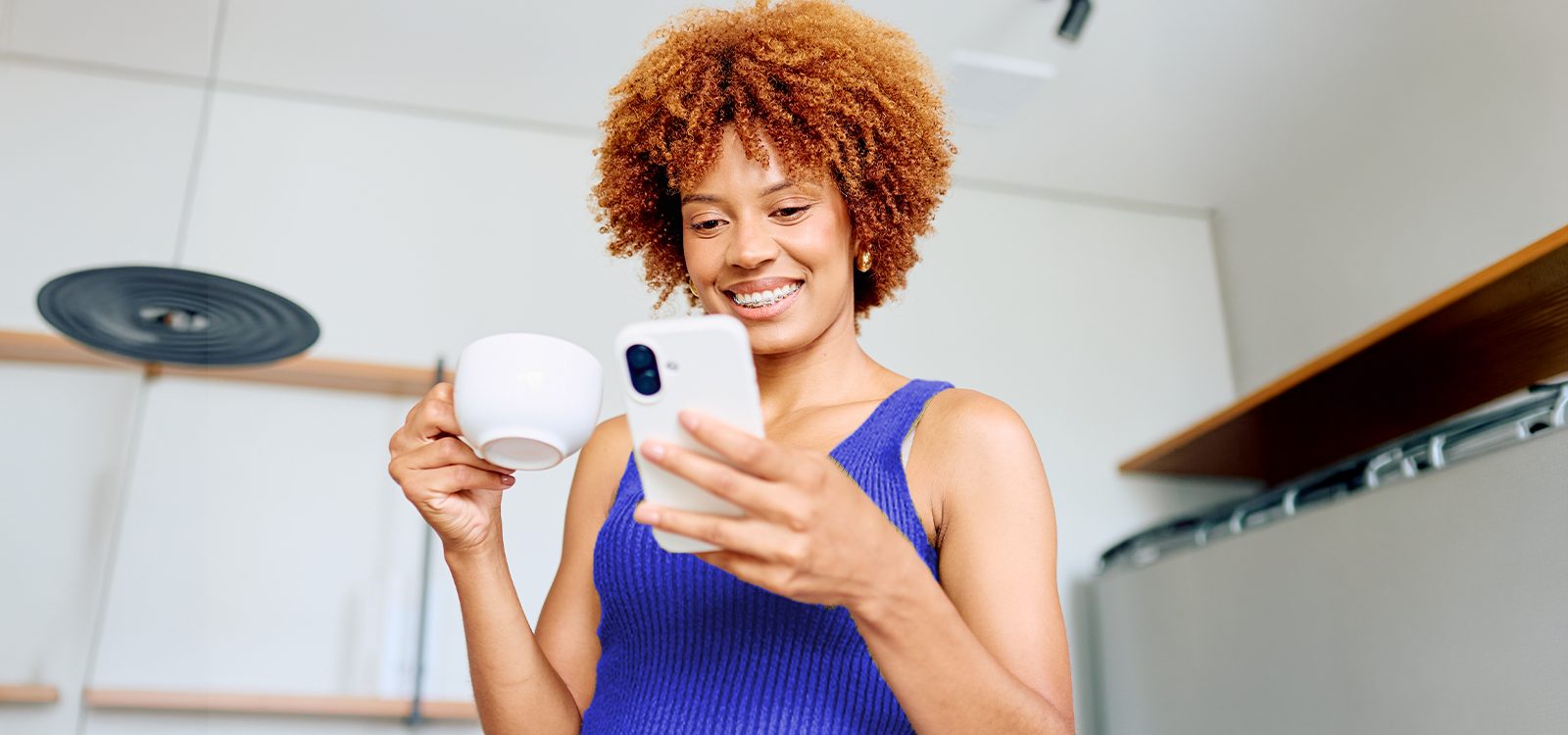 A woman looks at her smartphone while holding a cup of coffee