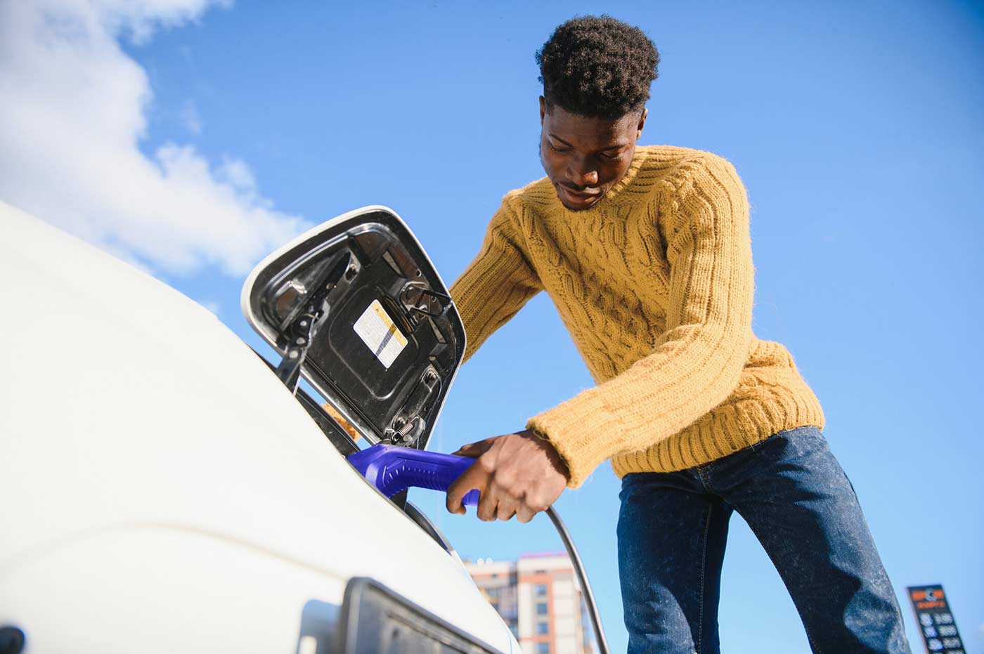 african man holding charge cable in on hand standing near luxury electric car.