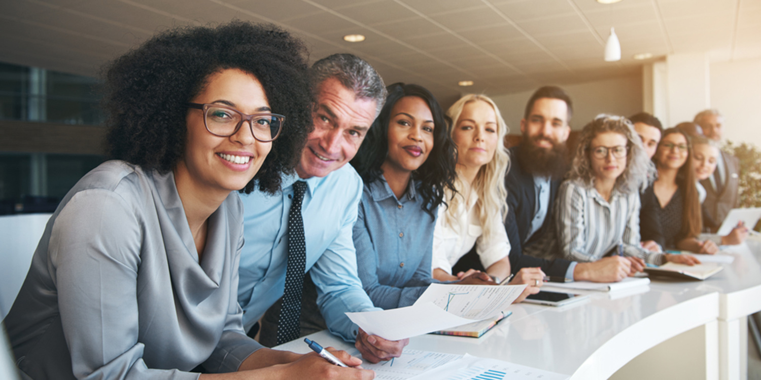 5 professional men and women sit at a conference table, looking at the camera