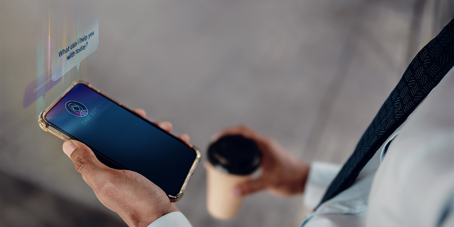 A man holds his smartphone in one hand and a cup of coffee in the other hand. There is a chatbot image displayed from the screen.
