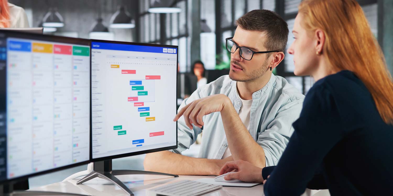 Two people look at a computer screen, discussing a topic