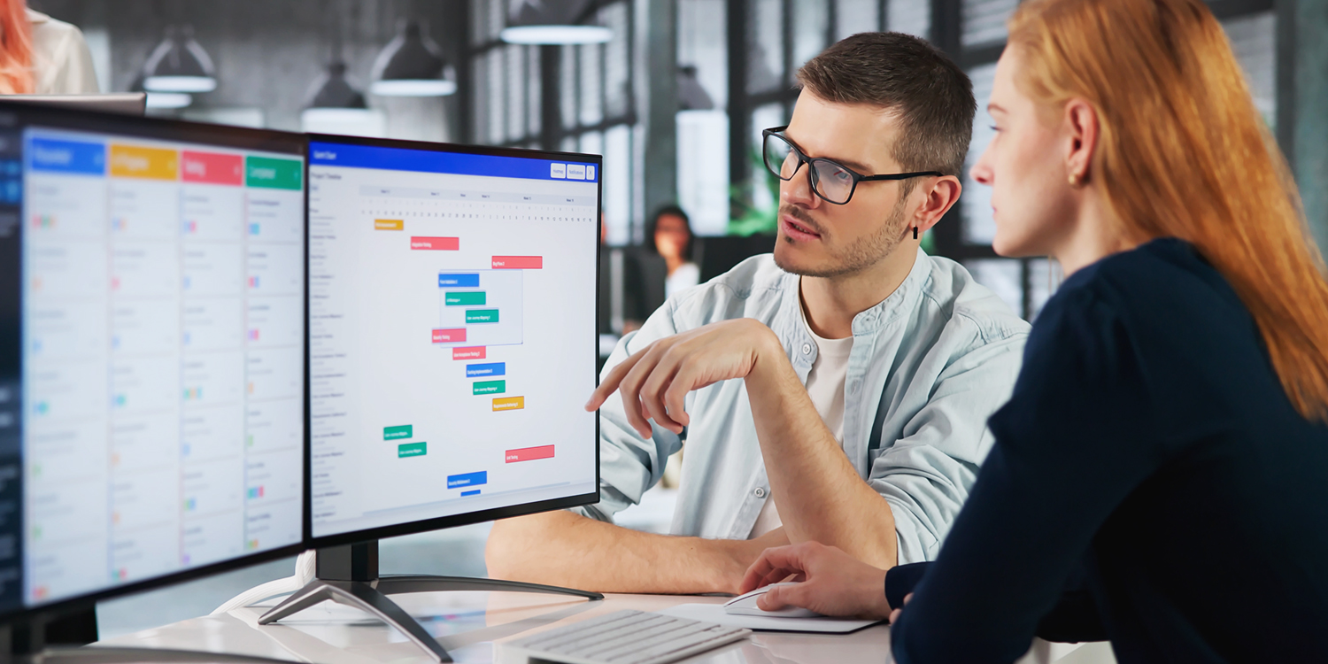 Two people look at a computer screen, discussing a topic