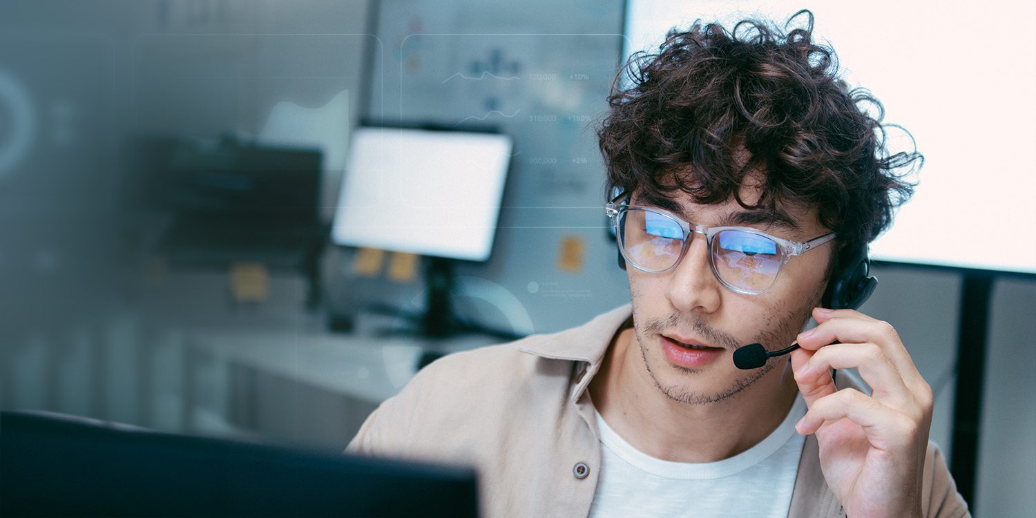 A man wearing a headset looks at a computer screen