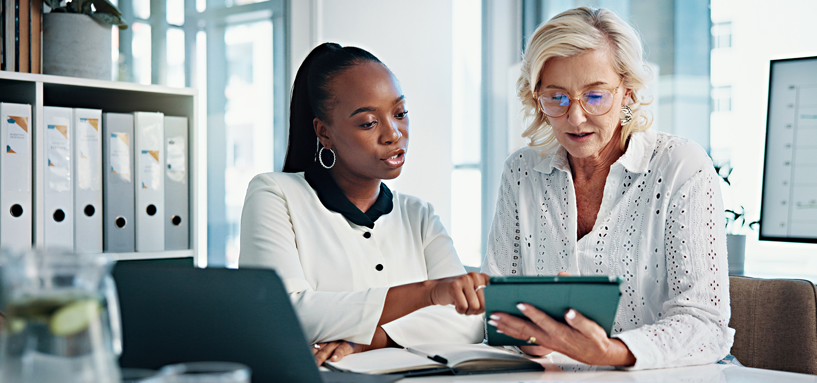 Two women in an office look at a digital notepad
